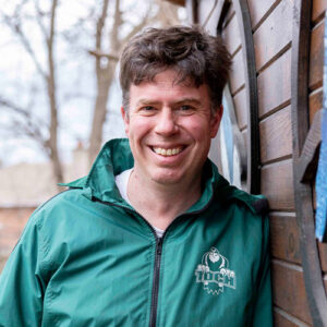 Photo of a man smiling wearing a greed TDCS jacket