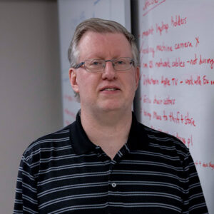 Photo of a man smiling standing in front of a whiteboard
