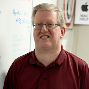 Photo of a man smiling in front of a whiteboard