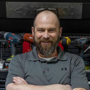 Photo of a man smiling, standing proudly in front of tools