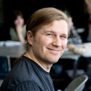 portrait of a smiling man in a black shirt with his hair tied back