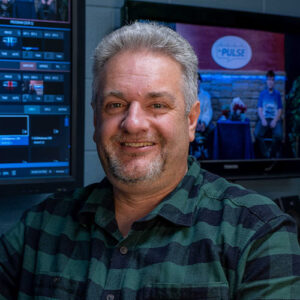 photo of a man smiling standing in front of computer monitors